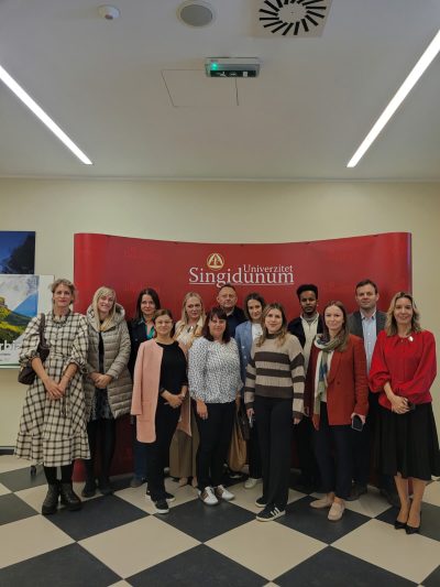 A group of diverse individuals poses together in front of a red banner with 'Singidunum University' written on it.